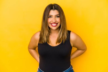 Sarı arka planda izole edilmiş genç Hintli kadın mutlu, güler yüzlü ve neşeli.