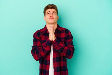 Mavi arka planda izole edilmiş genç beyaz bir adam el ele tutuşup, ağzının kenarında dua ediyor, kendinden emin..