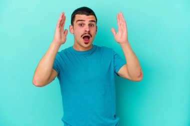 Kafkasyalı genç adam mavi arka planda izole edildi. Şaşırdı ve şok oldu..