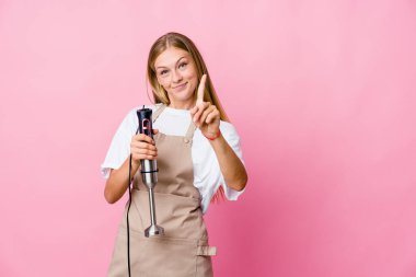 Genç Rus aşçı kadın bir elektrikli mikser tutuyor. Bir numarayı parmağıyla gösteriyor..