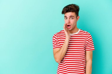 Mavi arka planda izole edilmiş genç beyaz bir adam gizli bir sıcak fren haberi veriyor ve yana bakıyor.