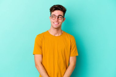 Mavi arka planda soyutlanmış genç beyaz bir adam gülümsüyor, neşeli ve keyifli görünüyor..