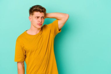 Kafkasyalı genç adam mavi arka planda izole edilmiş kafasının arkasına dokunuyor, düşünüyor ve bir seçim yapıyor..