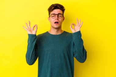 Sarı arka planda izole edilmiş genç beyaz adam sıkı çalışma gününden sonra rahatlıyor. Yoga yapıyor..