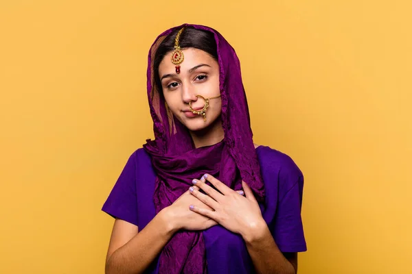 黄色の背景に隔離された伝統的なサリーを身に着けている若いインドの女性は 胸に手のひらを押して 優しい表情をしています 愛の概念 — ストック写真
