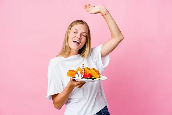 年轻的俄罗斯女人吃着一个被隔离的华夫饼 庆祝一个特殊的日子 跳跃着 精力充沛地举起双臂 — 图库照片