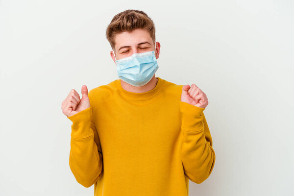 Young man wearing a mask for coronavirus isolated on white background raising fist, feeling happy and successful. Victory concept.