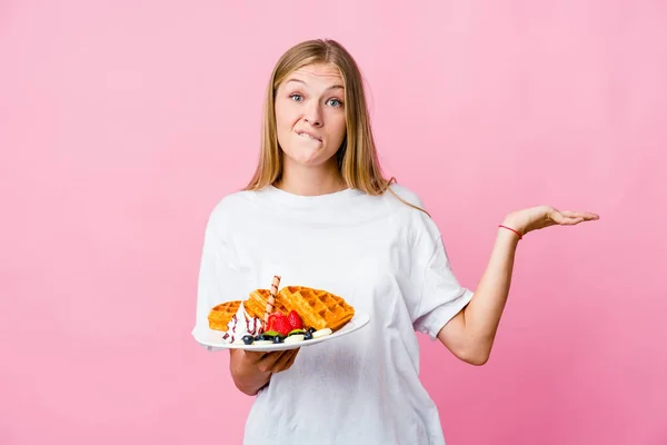Jovem Russa Comendo Waffle Isolado Confuso Duvidoso Ombros Encolhendo Para — Fotografia de Stock