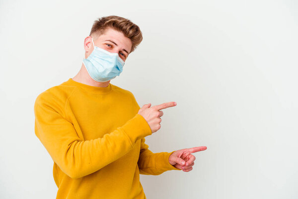 Young man wearing a mask for coronavirus isolated on white background excited pointing with forefingers away.
