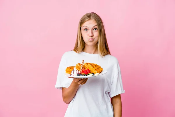 Young russian woman eating a waffle isolated blows cheeks, has tired expression. Facial expression concept.