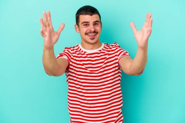 Mavi arka planda izole edilmiş genç beyaz bir adam zaferi ya da başarıyı kutluyor, şaşırıyor ve şok oluyor..