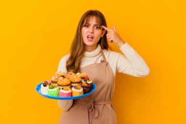 Sarı arka planda izole edilmiş genç pasta şefi kadın işaret parmağıyla bir hayal kırıklığı gösteriyor..