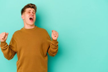 Mavi arka planda izole edilmiş genç beyaz bir adam zaferden sonra yumruğunu kaldırıyor, kazanan konsept..