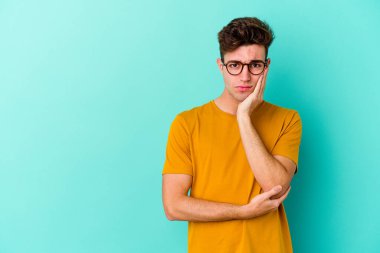 Mavi arka planda izole edilmiş, üzgün ve dalgın hisseden, kopyalama alanına bakan genç beyaz bir adam..