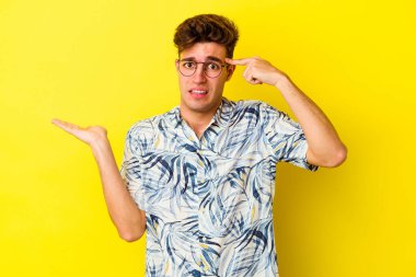 Genç beyaz adam sarı arka planda izole edilmiş ve elinde bir ürün var..