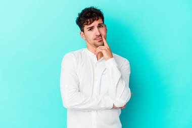 Mavi arka planda izole edilmiş genç beyaz adam alaycı bir ifadeyle kameraya bakarken mutsuz oluyor..
