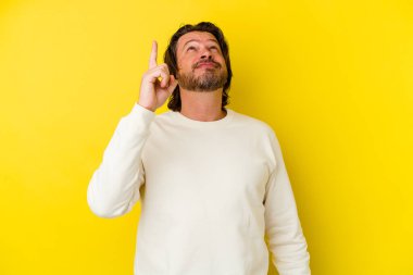 Sarı arka planda izole edilmiş orta yaşlı beyaz bir adam iki parmağı da boş bir alan gösteriyor..