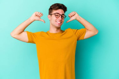 Mavi arka planda izole edilmiş genç beyaz adam gururlu ve kendinden emin hissediyor, örnek olarak.