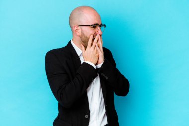 Genç, beyaz, kel bir adam mavi arka planda izole edilmiş. Bir şeye gülüyor, elleri ağızda..