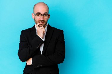 Kafkasyalı genç bir adam mavi arka planda izole edilmiş şüpheli ve şüpheci bir ifadeyle yana bakıyor..