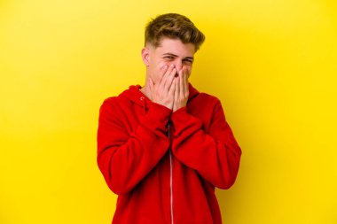 Sarı arka planda izole edilmiş genç beyaz bir adam bir şeye gülüyor, ağızlarını ellerle kapatıyor..