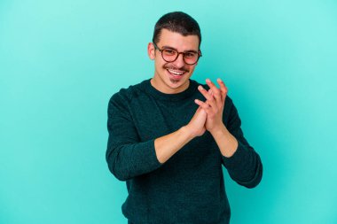 Kafkasyalı genç adam mavi arka planda izole edilmiş enerjik ve rahat hissediyor, ellerini ovuşturuyor kendinden emin.