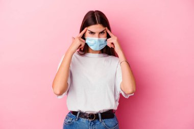 Pembe arka planda izole edilmiş virüs maskesi takan beyaz bir kadın bir göreve odaklanmış ve parmak uçlarını işaret ediyor..