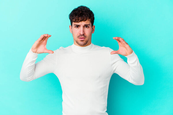 Молодой кавказский человек изолирован на синем фоне, держа что-то с ладонями, предлагая камере.