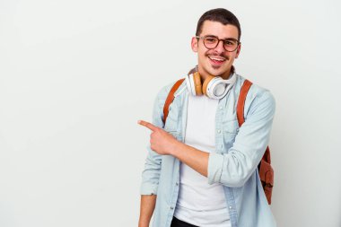 Beyaz arka planda izole edilmiş müzik dinleyen beyaz tenli genç bir öğrenci gülümsüyor ve boş alanda bir şeyler gösteriyor..