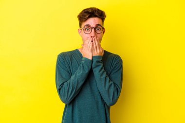 Sarı arka planda izole edilmiş genç beyaz adam elleriyle ağzını kapatırken şok oldu..