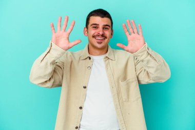 Mavi arka planda izole edilmiş genç beyaz adam on numarayı elleriyle gösteriyor..