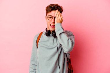 Pembe arka planda izole edilmiş genç bir öğrenci yüzünün yarısını avuç içiyle kaplayarak eğleniyor..