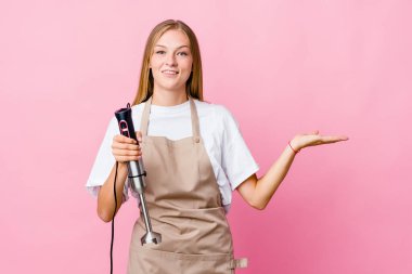 Genç Rus aşçı kadın, elinde elektrikli mikser tutarken kollarıyla ölçeği yapıyor, mutlu ve kendinden emin hissediyor..