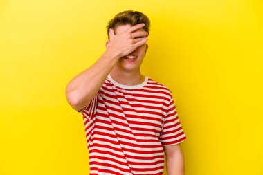Sarı arka planda izole edilmiş genç beyaz adam elleriyle gözlerini kapatıyor, geniş bir gülümsemeyle bir sürpriz bekliyor..