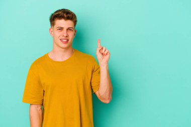 Mavi arka planda izole edilmiş genç beyaz adam bir numarayı parmağıyla gösteriyor..