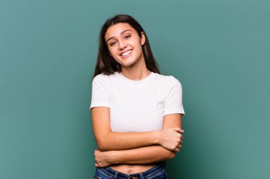 Genç Hintli bir kadın mavi arka planda izole edilmiş, kendinden emin, kararlılıkla kollarını kavuşturan.