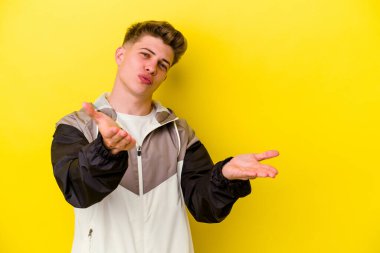 Sarı arka planda izole edilmiş genç, beyaz bir adam. Dudaklarını kıvırıyor, avuç içlerini tutuyor ve hava öpücüğü yolluyor..