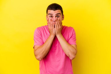 Sarı arka planda izole edilmiş, ağzı ellerle kaplanmış, yeni bir şey keşfetmeye hevesli genç beyaz bir adam..