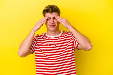 Kafkasyalı genç adam sarı arka planda izole edilmiş, başı ağrıyor, yüzüne dokunuyor..