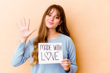 Genç beyaz kadın, elinde aşk levhasıyla izole edilmiş gülümseyen beş numarayı parmaklarıyla gösteriyor..