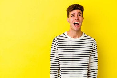 Sarı arka planda izole edilmiş genç beyaz bir adam çok kızgın, öfkeli, hayal kırıklığına uğramış diye bağırıyor..