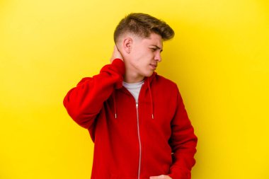 Sarı arka planda izole edilmiş genç beyaz bir adam stresten dolayı boynu ağrıyor, masaj yapıyor ve elle dokunuyor..