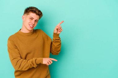Kafkasyalı genç adam mavi arka planda izole edilmiş. İşaret parmağıyla işaret ettiği için heyecanlı..