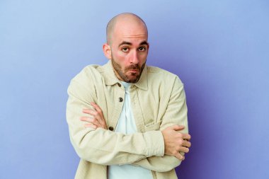 Mor arka planda soyutlanmış beyaz kel bir adam omuzlarını silker ve gözleri açık kalır..