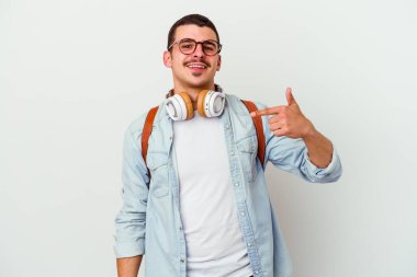 Beyaz arka planda izole edilmiş müzik dinleyen beyaz tenli genç beyaz bir öğrenci gömlek fotokopi alanını işaret ediyor, gururlu ve kendinden emin.