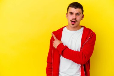Sarı arka planda izole edilmiş genç beyaz adam yan tarafı işaret ediyor.
