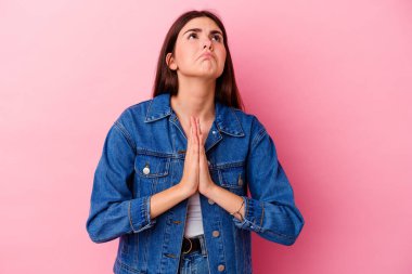 Pembe arka planda soyutlanmış genç beyaz bir kadın el ele tutuşup ağzının kenarında dua ediyor, kendinden emin hissediyor..