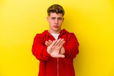 Sarı arka planda izole edilmiş genç beyaz adam inkar jesti yapıyor.