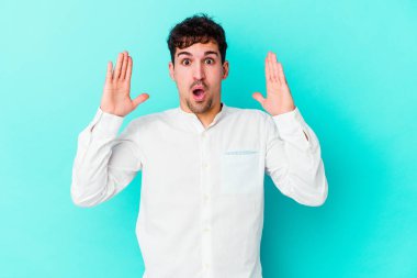 Kafkasyalı genç adam mavi arka planda izole edildi. Şaşırdı ve şok oldu..