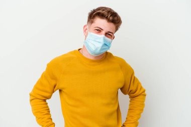 Koronavirüs maskesi takan genç adam beyaz arka planda izole edilmiş, kendine güveni tam, kalçaları tutuyor..